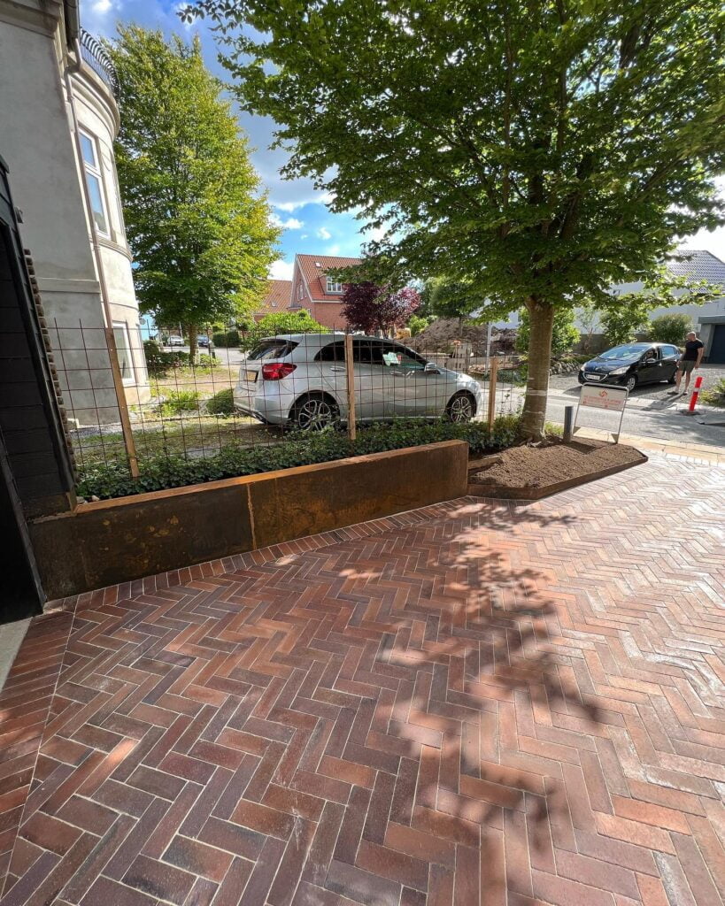 Ny brolægning foran hus med parkerede biler